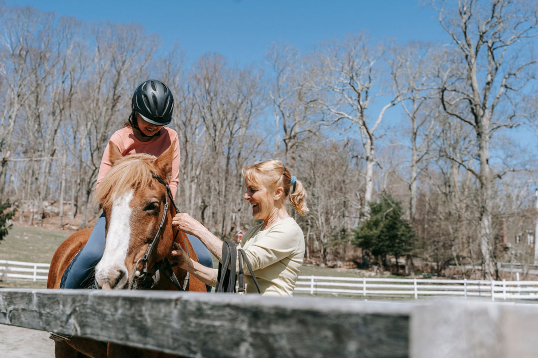 Riding instructor adjusting a child's stirrup during a pony lesson in an outdoor arena